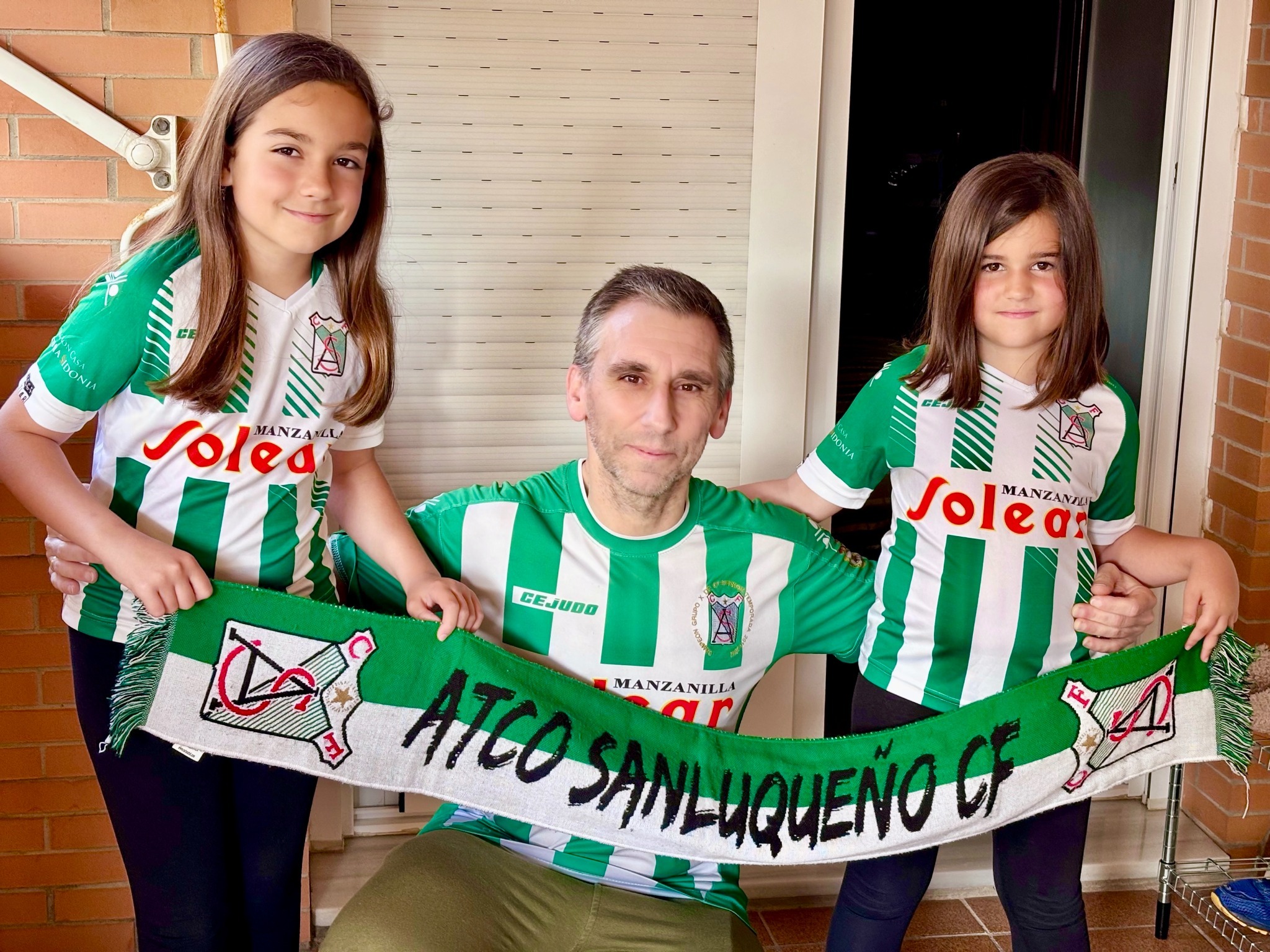 Rafa con sus hijas mostrando los colores y la bufanda del Atlético Sanluqueño CF
